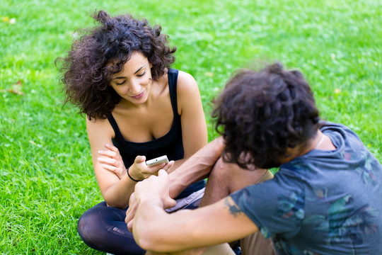 一对拉丁夫妇拿着电话坐在草地上