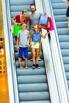 一家人在购物中心的自动扶梯上提着包