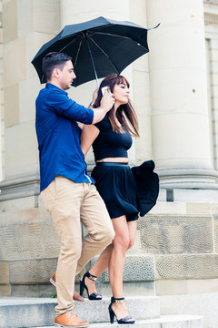 年轻人拿着雨伞和手机靠近女友的耳朵