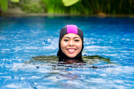 穿着布基尼清真泳衣在热带花园游泳池游泳的穆斯林妇女或女孩