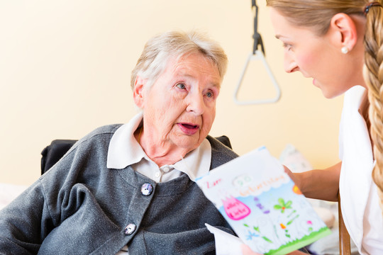 护士给坐在轮椅上的养老院老年妇女送生日卡