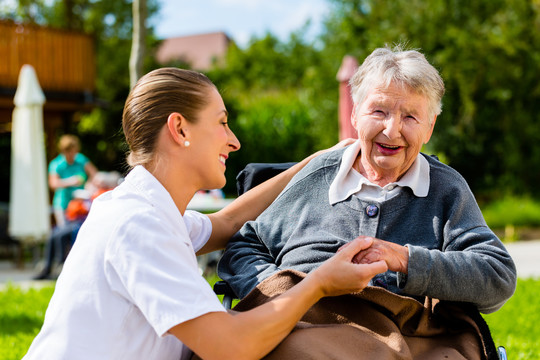 在养老院的花园里，护士和坐在轮椅上的老年妇女手牵手