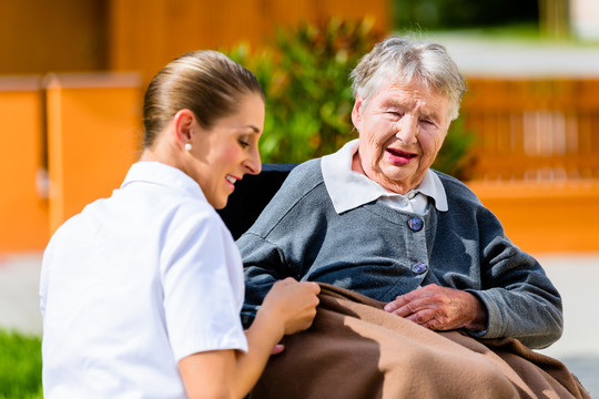 在养老院的花园里，护士和坐在轮椅上的老年妇女手牵手