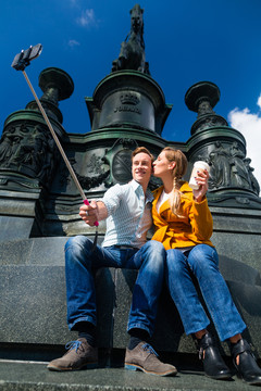 在德累斯顿剧院广场上，一对旅游情侣手持手机在自拍