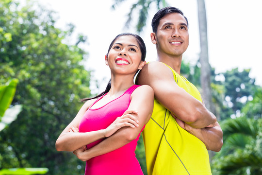 亚洲女子和男子在慢跑训练中肩并肩站在热带公园观看比赛