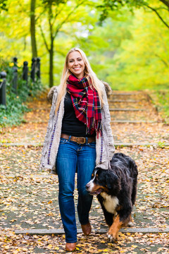 在公园里，一个女人牵着狗走在一条覆盖着彩色秋叶的小路上