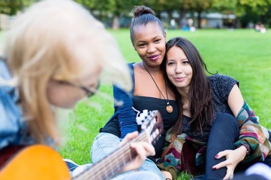 朋友们在公园里唱歌，和一个弹吉他的女孩一起玩，这是一个由非洲、亚洲和高加索人组成的多元化团体