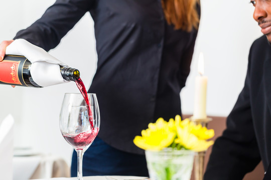 在一家高档餐厅，女服务员正在往玻璃杯里倒酒
