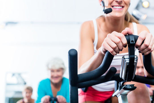 老年人和年轻人在健身房骑健身自行车进行耐力和有氧运动训练，教练正在引导他们