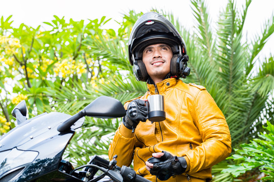 骑摩托车、戴头盔的亚裔男子在休息时间喝咖啡