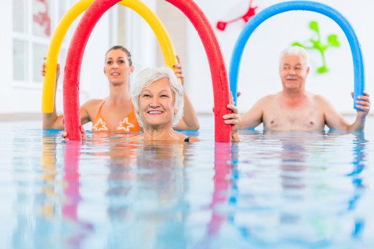 团体或年轻人和老年人在水溶性健身游泳池用泳池面条锻炼