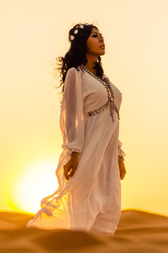 美丽的女孩站在沙漠的夕阳下