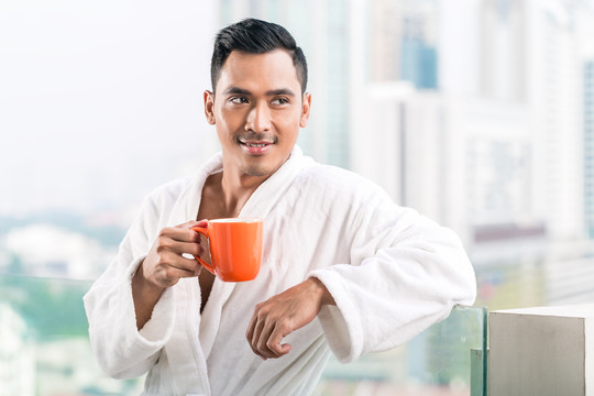 亚洲男子早上在城市天际线前喝咖啡