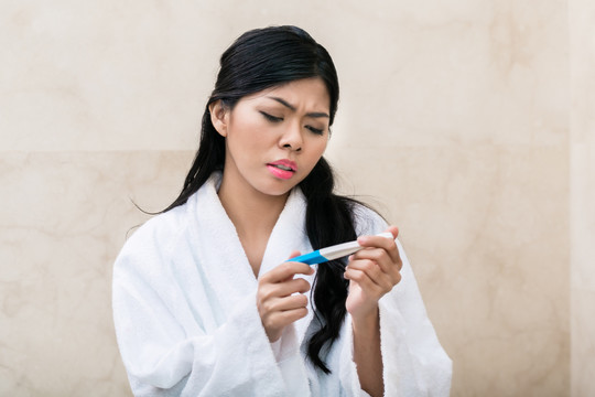 一名亚洲妇女在早上检查怀孕测试时感到悲伤