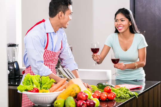 亚洲夫妇，丈夫和妻子，在厨房准备晚餐和喝红酒