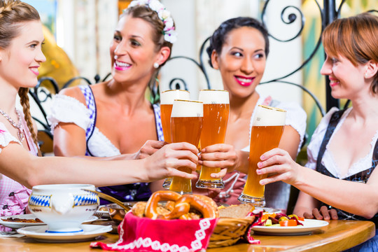 巴伐利亚酒馆里的女孩们在椒盐卷饼前用小麦啤酒祝酒