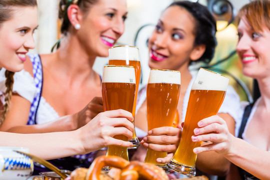 巴伐利亚酒馆里的女孩们在椒盐卷饼前用小麦啤酒祝酒