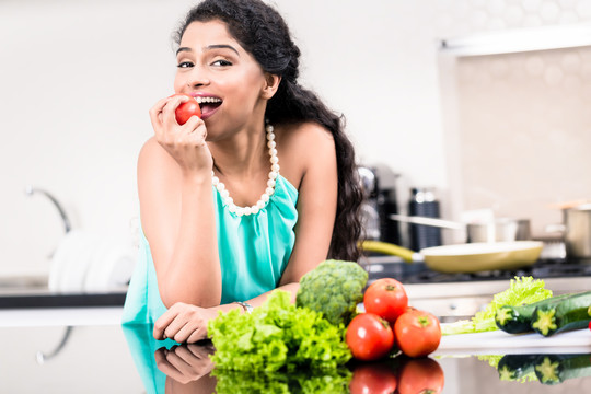 一名印度妇女在厨房里吃健康的苹果，在柜台上吃沙拉和蔬菜