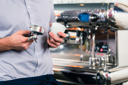 在自动咖啡机上准备浓缩咖啡的服务员的手的特写镜头