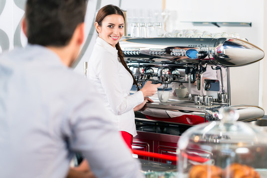 在室内自动咖啡机旁准备浓咖啡时，迷人的女服务员对男顾客微笑