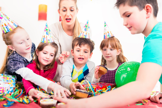 在生日派对上，孩子们抓着松饼和蛋糕，戴着帽子、气球和纸带装饰