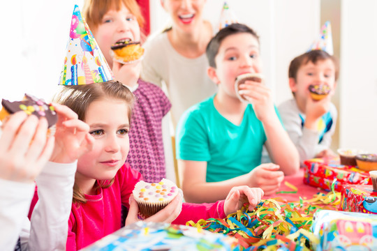 孩子们在生日聚会上抓着松饼和蛋糕，孩子们戴着帽子、气球和纸带装饰