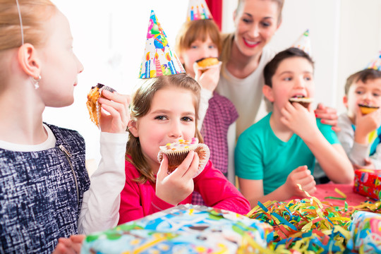 孩子们在生日聚会上抓着松饼和蛋糕，孩子们戴着帽子、气球和纸带装饰