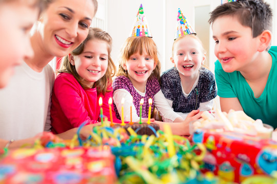 在朋友和母亲的帮助下，孩子在生日派对上吹蛋糕上的蜡烛