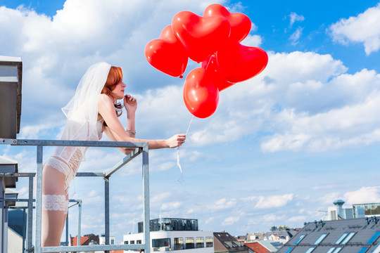 穿着内衣在阳台上戴着红气球的新娘