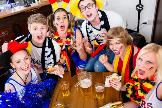 体育酒吧里的足球迷们穿着旗子和化妆品兴奋地观看比赛