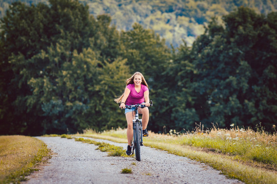夏天，一个骑自行车的女孩在一条泥泞的小路上骑车，背景是树林