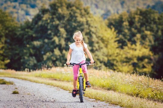 夏天，一个骑自行车的女孩在一条泥泞的小路上骑车，背景是树林