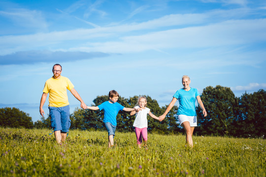 一家人手牵着手在草地上奔跑，母亲、父亲和孩子们