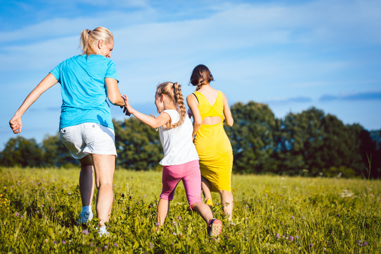 两个女人和一个女孩在夏天的草地上嬉戏奔跑