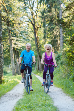 一对快乐活泼的老年夫妇穿着酷炫的健身服，在公园户外骑自行车