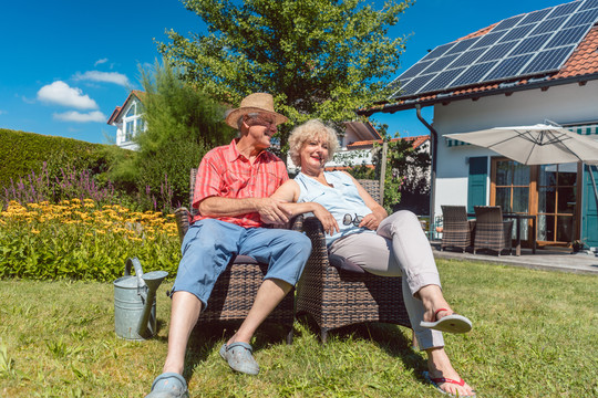 一对相爱的快乐老年夫妇坐在椅子上，在夏日阳光明媚的日子里，一起在家里的花园里放松的低角度照片