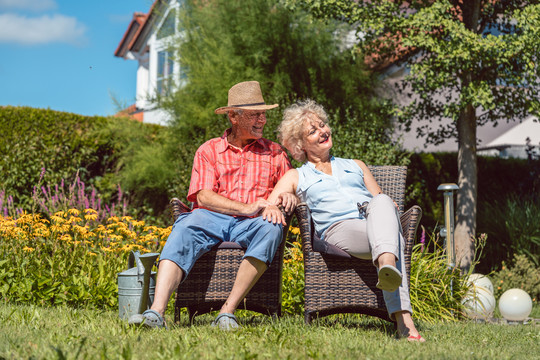 在阳光明媚的夏日里，一对幸福的相爱的老年夫妇坐在椅子上，一起在花园里放松时的低角度视图肖像
