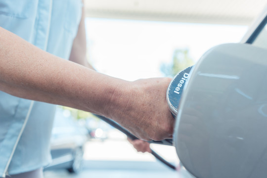 在加油站为汽车加油时，一位老妇人手拿着加油泵的侧面特写镜头