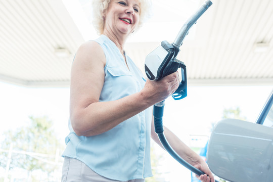 一名高级女司机在加油站加油前手持加油机的手的特写镜头