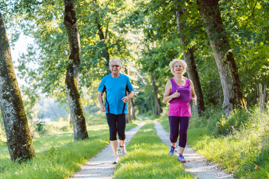 两位活跃的老年人在公园户外慢跑时面带微笑的健康生活方式的全幅正面视图