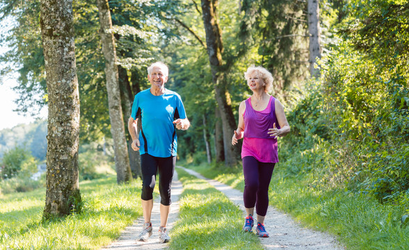 两位活跃的老年人在公园户外慢跑时面带微笑的健康生活方式的全幅正面视图