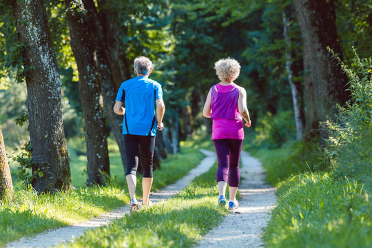 夏日，一对穿着酷炫跑步服的老年夫妇在公园田园诗般的小路上一起在户外慢跑时的全幅后视图