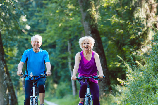 一对快乐活泼的老年夫妇穿着酷炫的健身服，在公园户外骑自行车