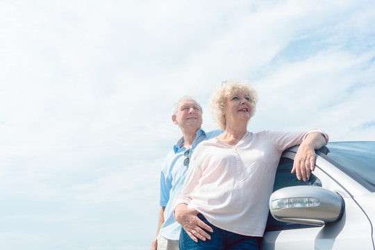 两位老年人靠在车上微笑着，带着自信和积极的态度望向别处的低角度照片