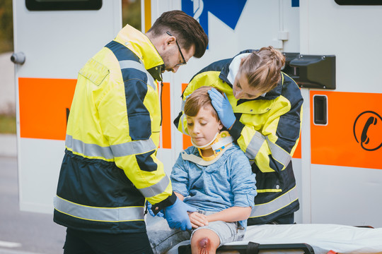 男孩在事故后受伤，医护人员在救护车前照顾他
