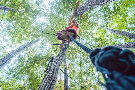 非常健康和运动型的女人攀爬绑在树上的绳子