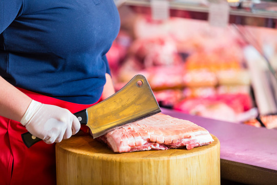 屠夫用大刀在一块肉上切肉
