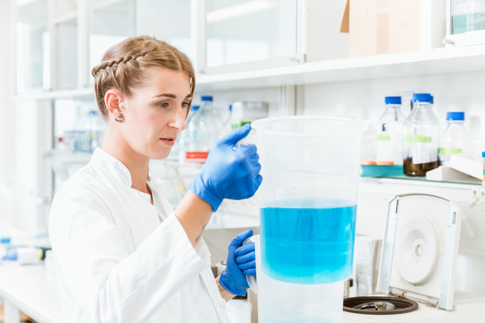 年轻专注的女医生在实验室进行实验时，看着烧杯中的蓝色液体
