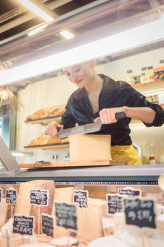 熟食店的年轻店员在柜台上用刀切奶酪