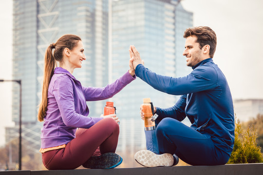 在一座城市里，一位女士和一位男士在健身运动后打招呼，背景是一座高层建筑